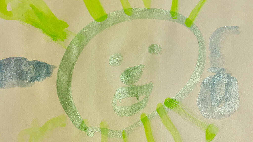 Pintura infantil de una cara redonda amarilla con una sonrisa sencilla, dos ojos y rayos de sol —que trae alegría durante la COVID-19— junto a formas azules en el lateral, todo sobre papel blanco.